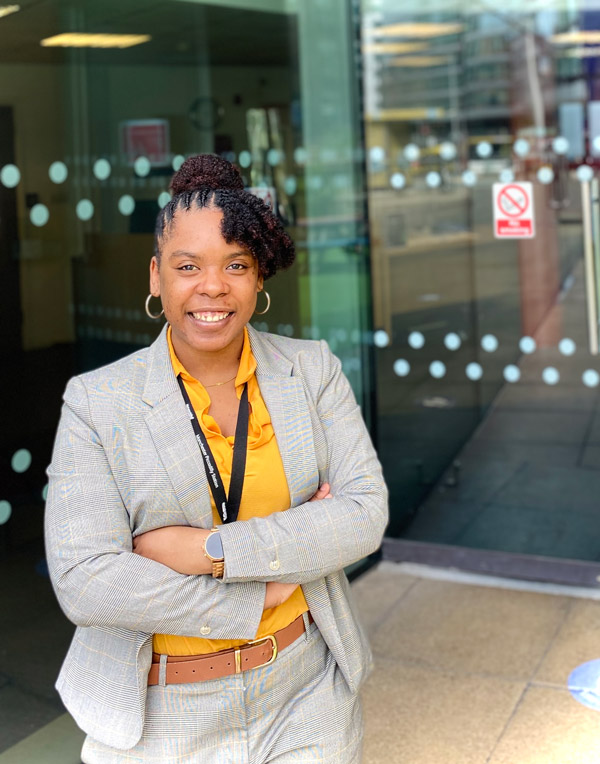 Chelset smiling to the camera wearing a suit and bright yellow blouse