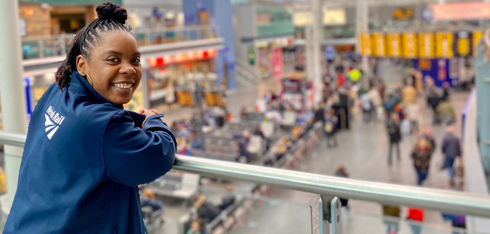 A female wearing a Network Rail jacket looking over a balcony down to a busy station concourse