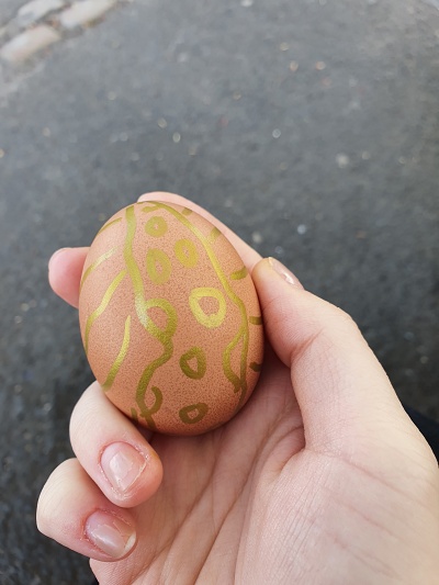 Hand holding an egg with gold paint in spirals