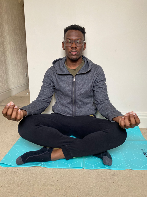 A male student sitting on a yoga mat, crossed legs with eyes closed