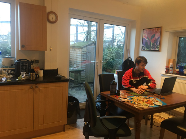 A student sitting at a kitchen table working on a laptop