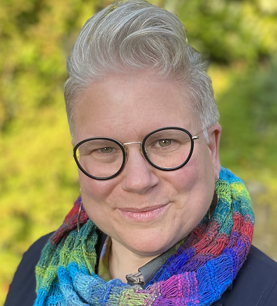 Claire stands outside wearing a colourful scarf and glasses.
