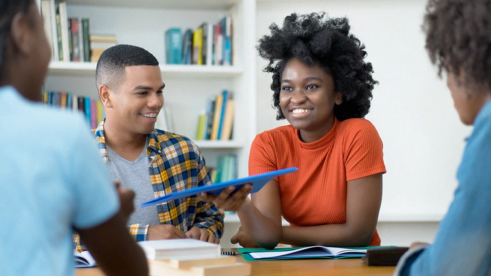 A group of people sit around a table talking, The picture focuses on an individual with afro-texture
