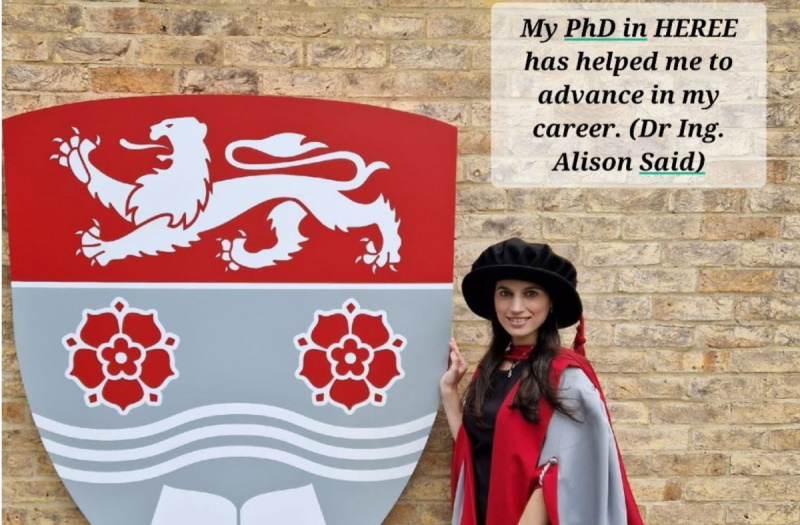 Alison Said standing next to large LU crest.  Text in image is "My PhD in HEREE has helped me to advance in my career. Dr Ing. Alison Said"