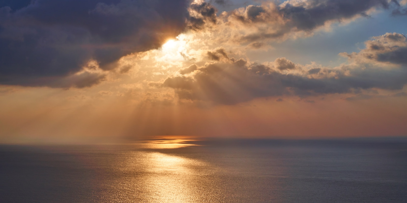 Sun setting over the sea with sunrays seen through clouds.