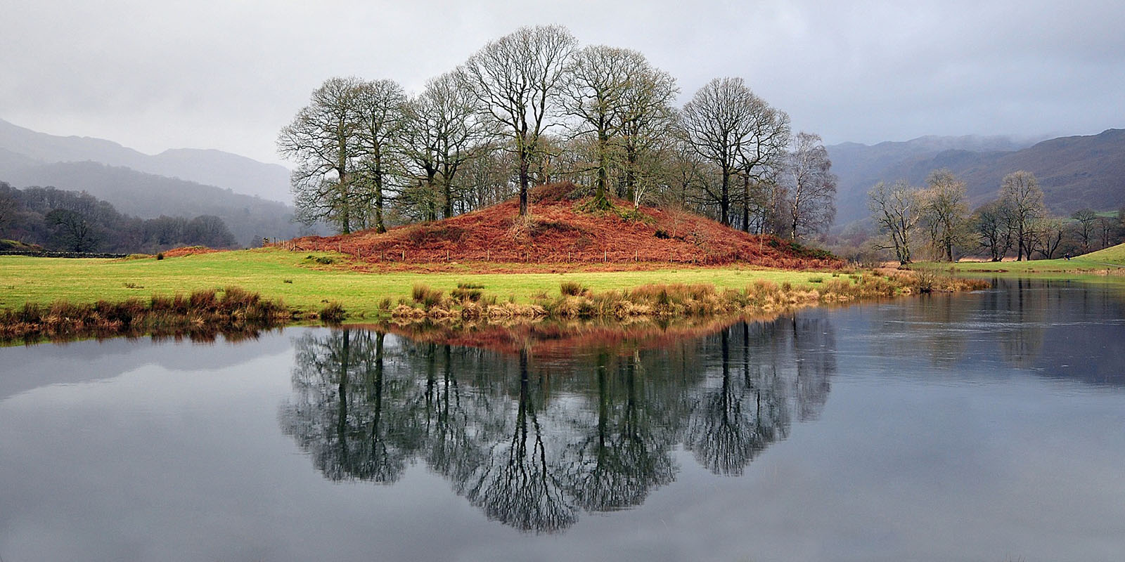 An island with trees reflected in the lake in the foreground.