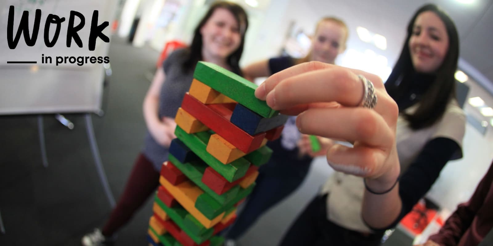 People playing Jenga. Work in Progress logo in the corner.