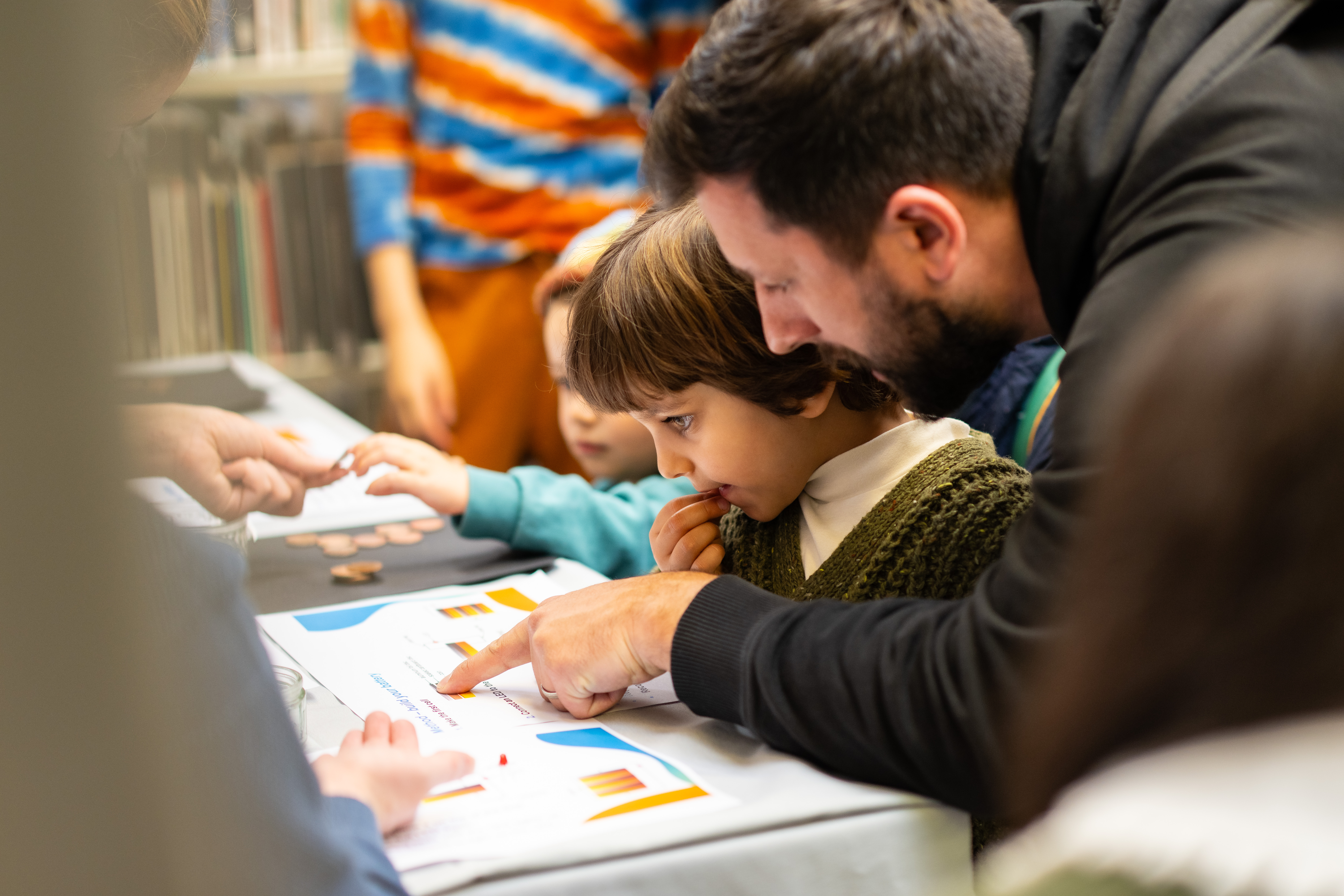 a parent and a child look at some information on a deak with the father pointing at something