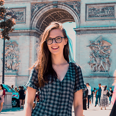 Rebecca smiling into the camera, standing in front of a colourful archway.