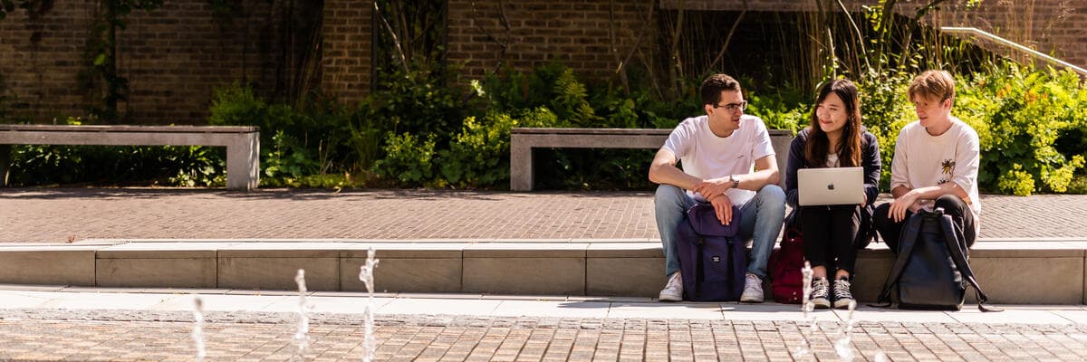 Three people sat on the steps next to the fountains by the great hall