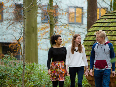 Three students walking along a green wooded path.