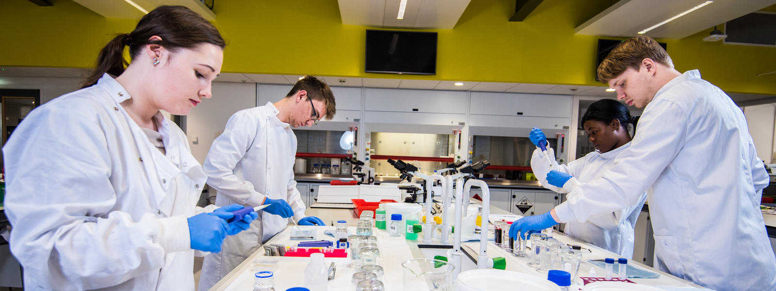 Multiple students are working at a central laboratory table