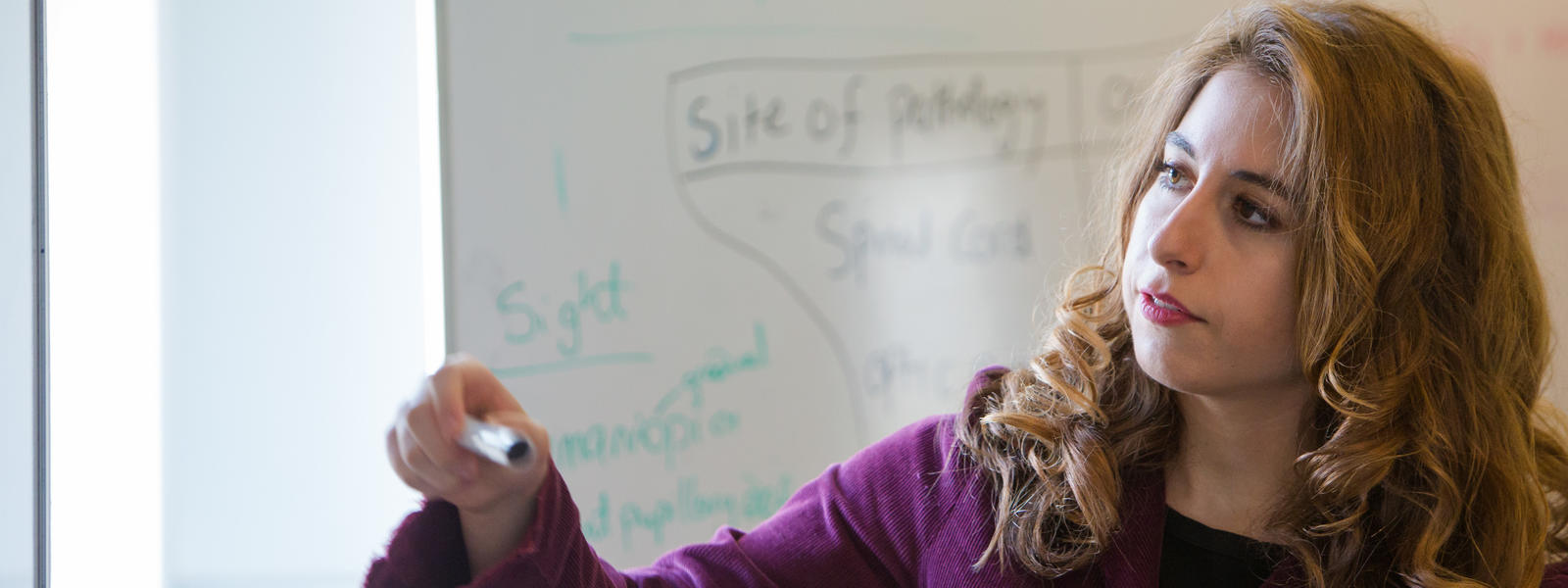 A student looks to the left, holding a pen