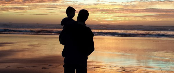 Parent and child silhouetted against beach sunset