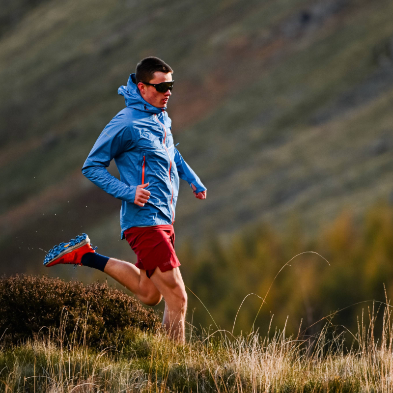 Isaac is running in nature while wearing a blue jacket and red shoes 