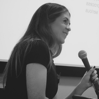 Laura O'Donovan speaking at an event, holding a microphone and smiling