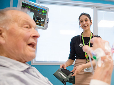 An elderly man in a hospital bed with a nurse nearby