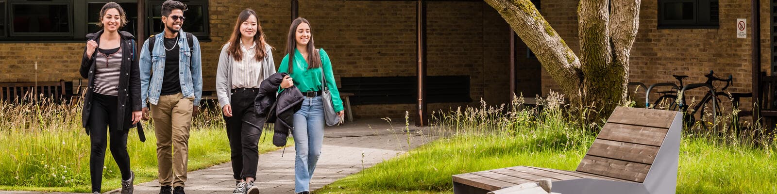 Four students walking together through the path in Bowland Quad with grass on either side.