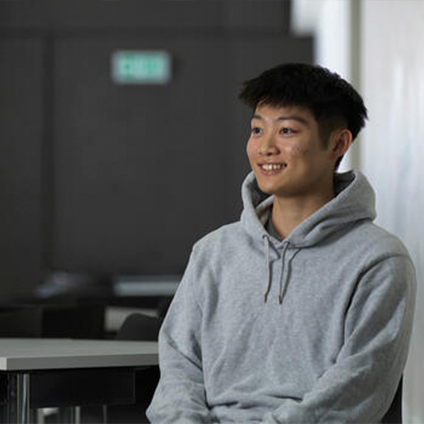Student in a grey jumper smiling at a camera
