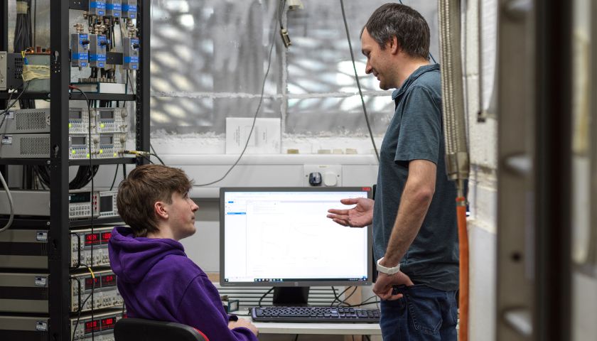 A student and an academic sat at a computer by the 1978 fridge