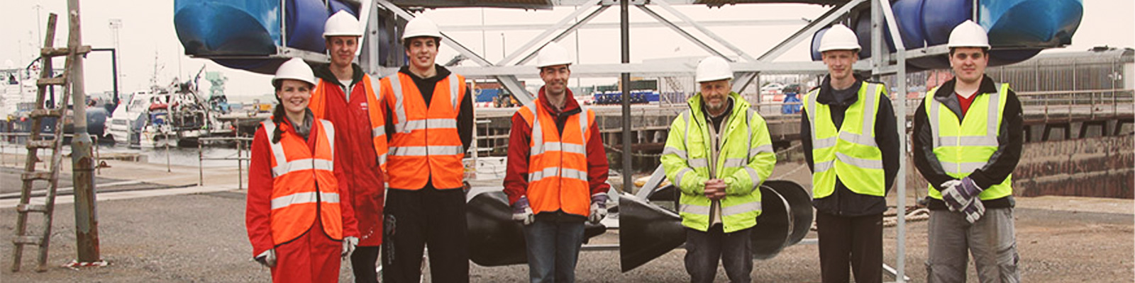 Engineering students in high visibility work clothing stand around a heavy piece of apparatus.