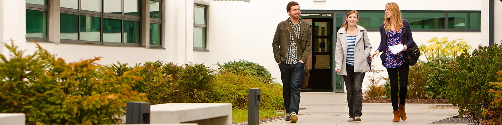 Three students cross an open area between buildings in the Lancaster Environment Centre