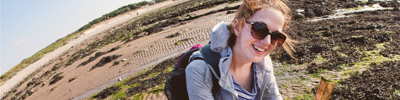 A student on a field trip collects samples from a beach