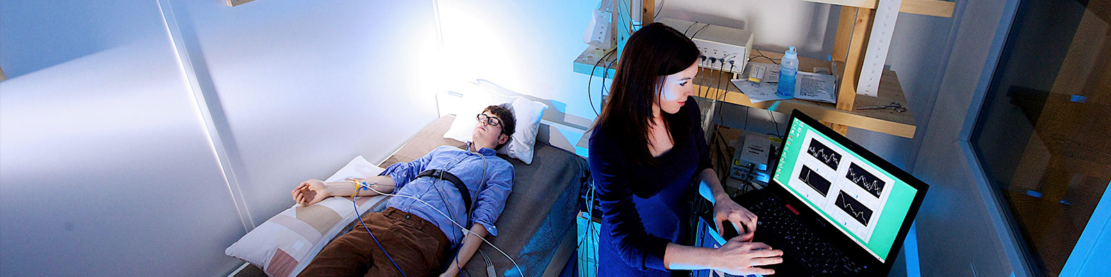A man lies on a bed whilst a student monitors aspects of his health