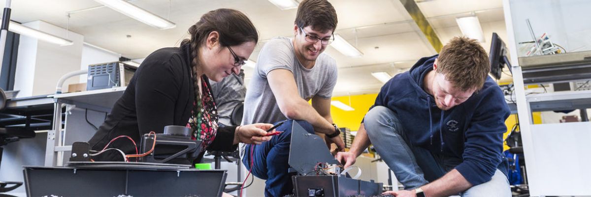 Three people examining a robot