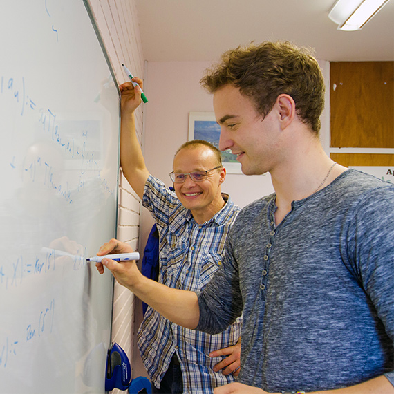 Two people writing on a whiteboard