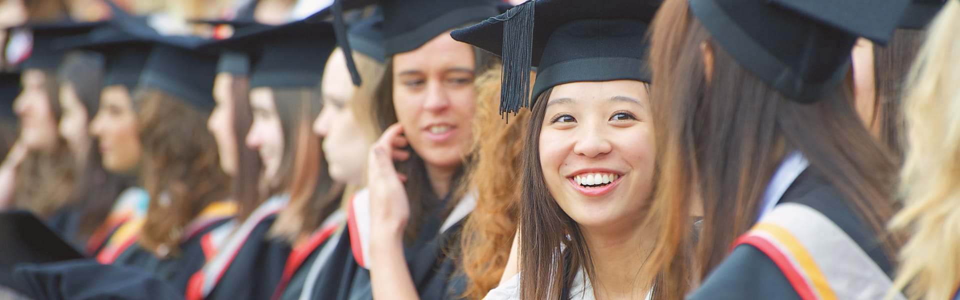 A group of smiling students in caps and gowns await a graduation photograph.