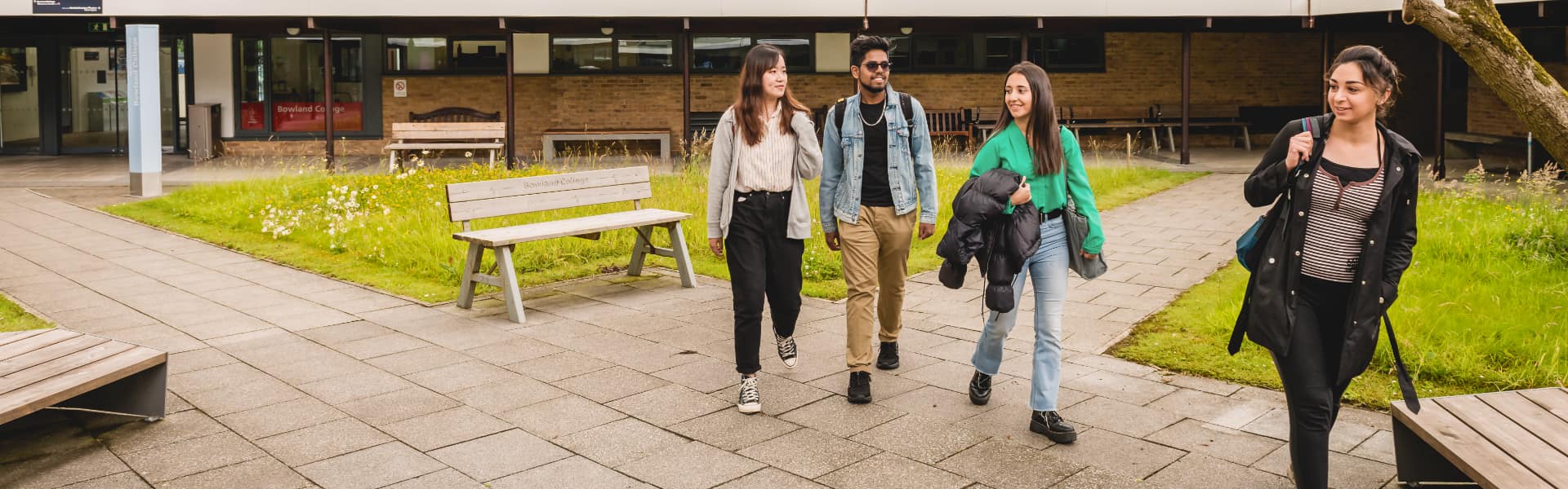 4 students walk across the campus, surrounded by greenery.