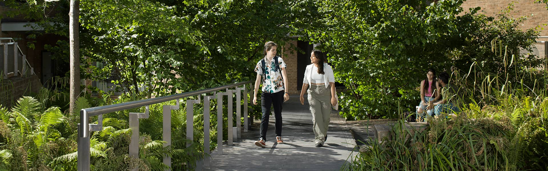 Two students walk and chat surrounded by greenery on a sunny day