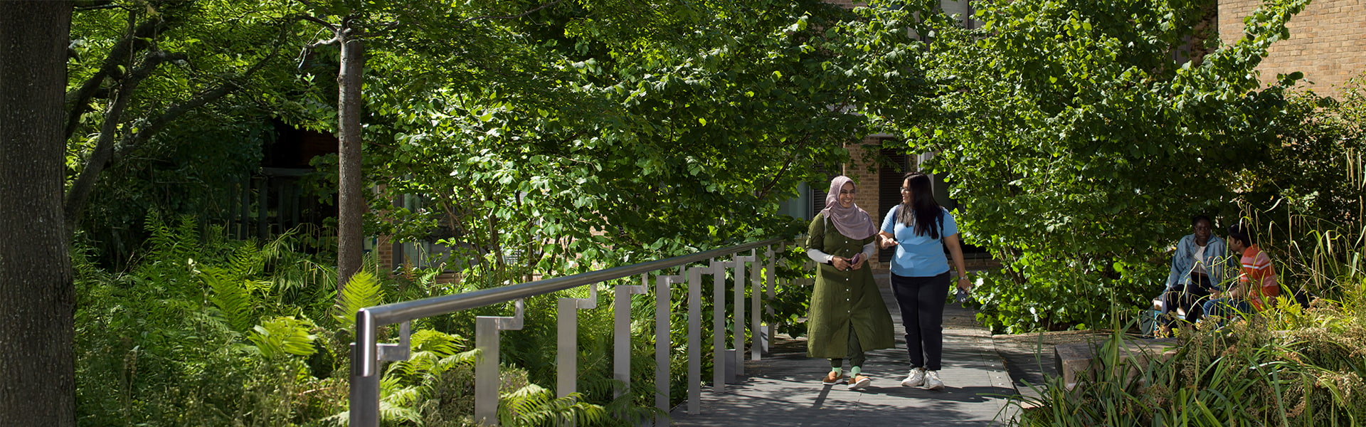 Two students walking through the trees by the great hall.