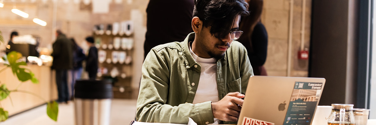 A young man sits in a bright and airy cafe using a laptop computer