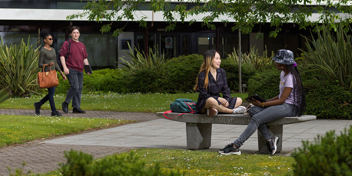 Two students standing outside the Management School with directional signs