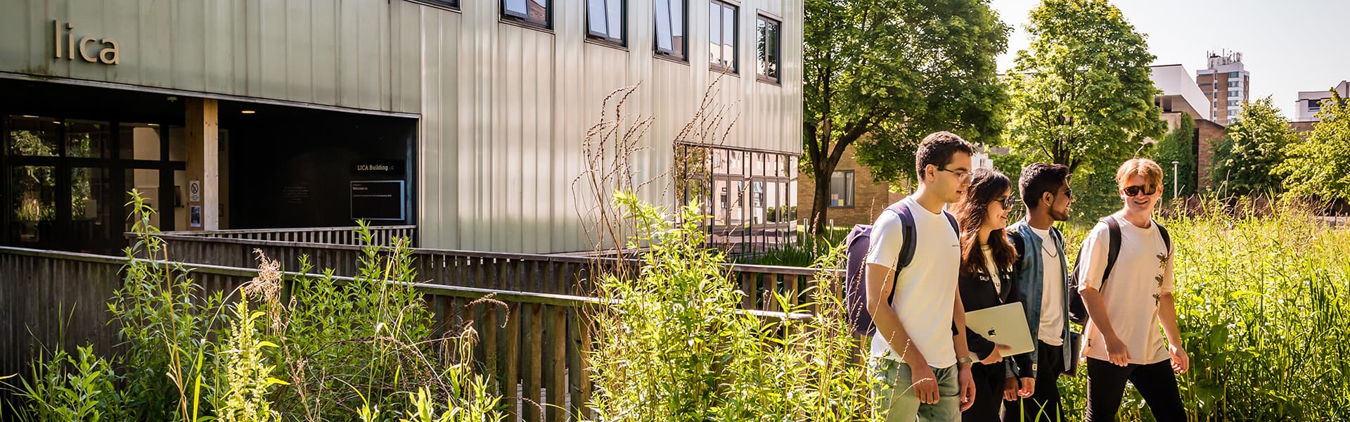 Students leaving Lancaster's LICA building via a wooden bridge, surrounded by greenery