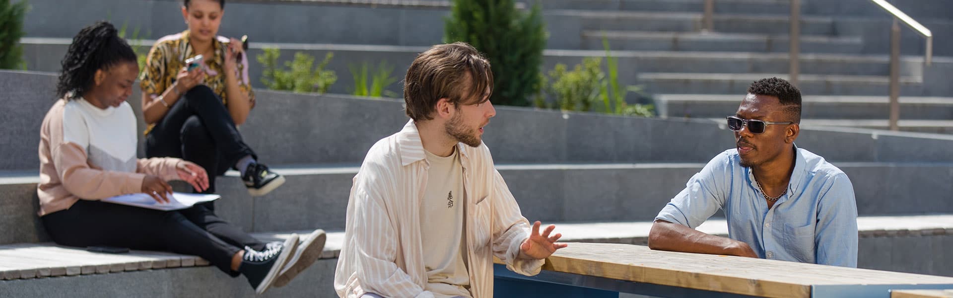 Students seated in a outdoor courtyard chatting and looking at laptops