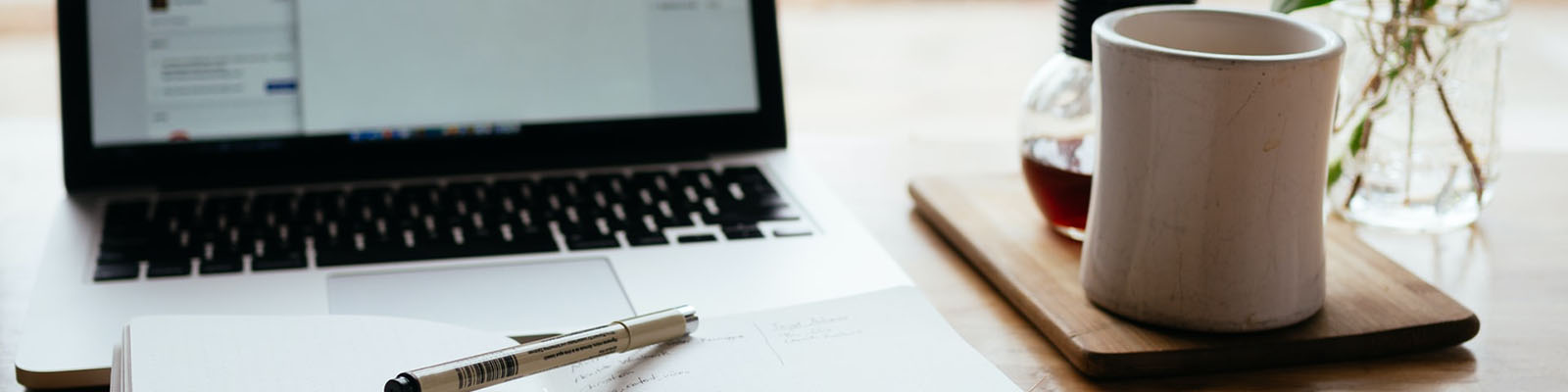 A laptop with a notepad and pen on it.