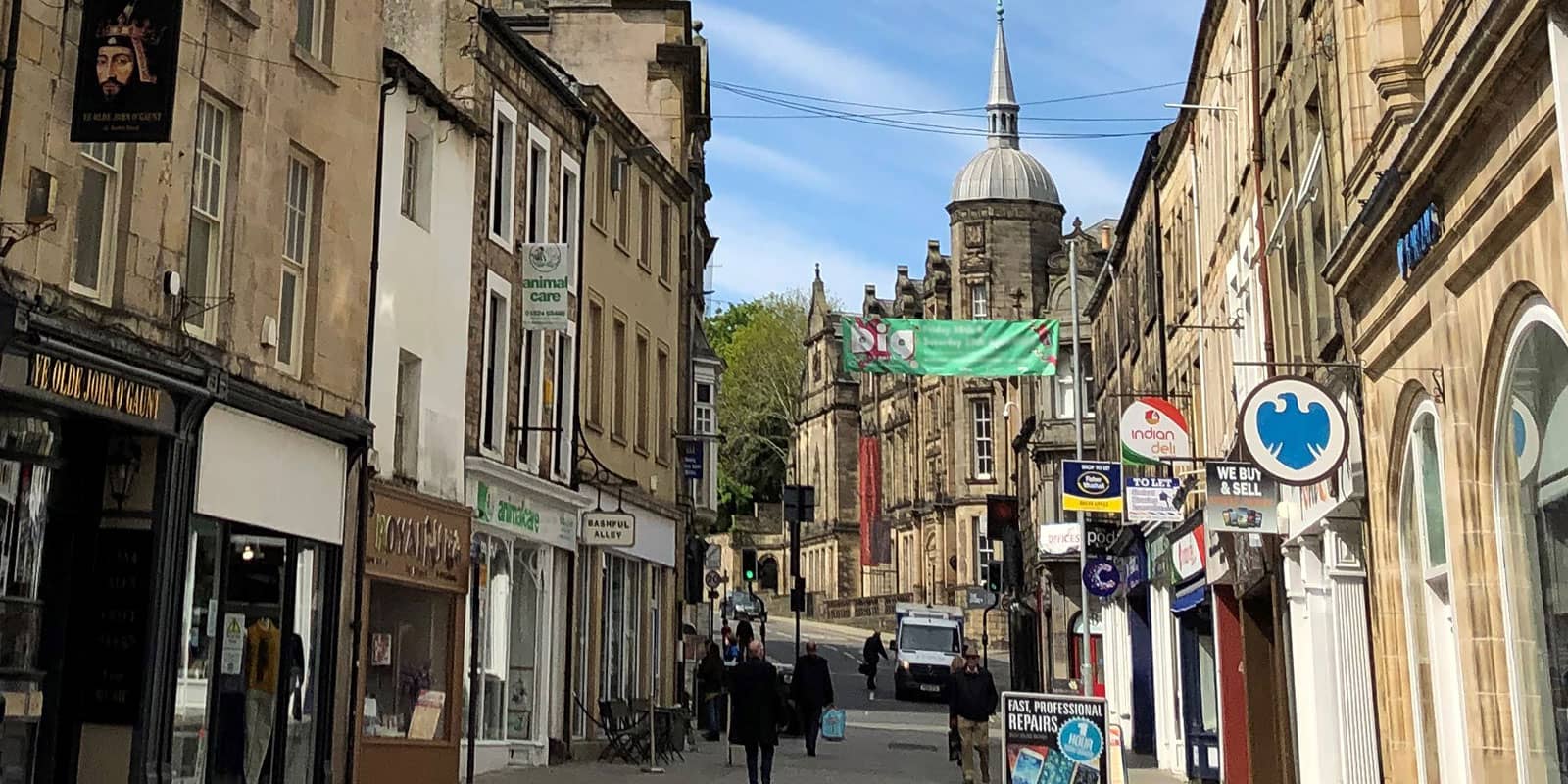 Lancaster city street, the old buildings made from Millstone Grit, is filled with shops and some shopers.