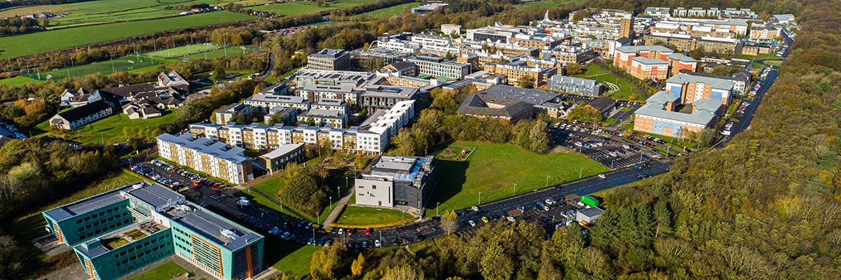 Aerial photograph of the campus, with woodlands surrounding it and Morecambe Bay in the distance.