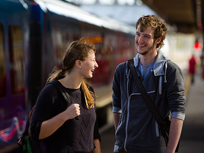Two people at the train station, with a train, stopped at the platform.