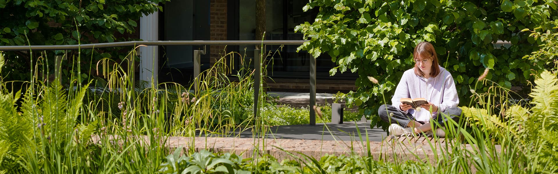 A student sits reading surrounded by greenery
