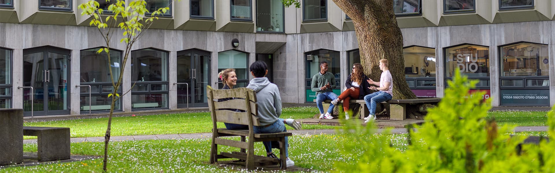 Students leaving Lancaster's LICA building via a wooden bridge, surrounded by greenery