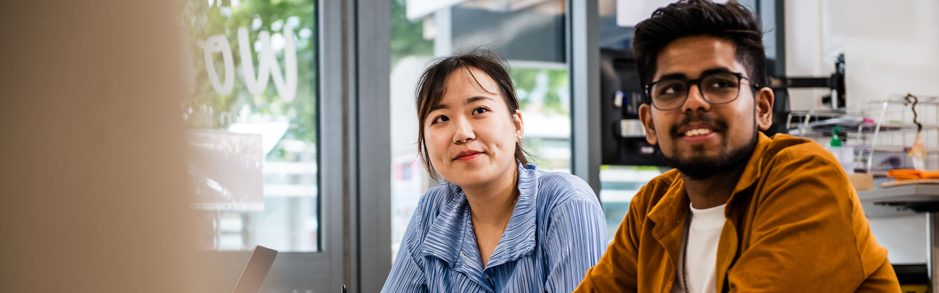 Two students look at something beyond the frame of the image, such as a whiteboard or a lecturer