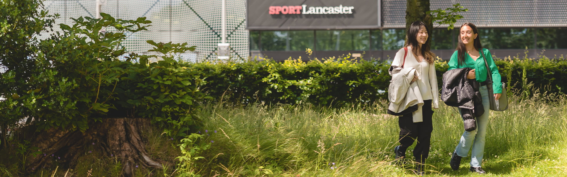 Two students walking through some greenery near the Sports Centre