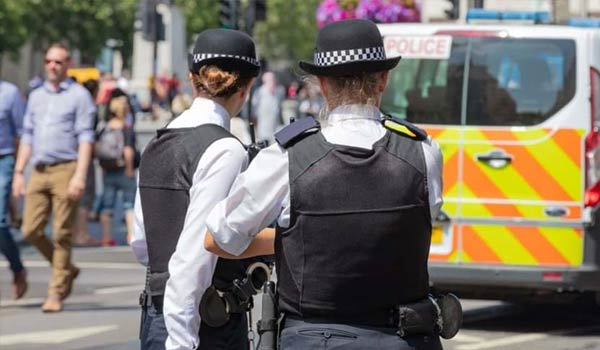 Rear view of Two Female Metropolitan Police Officers in the Street. Unfocused Police Van Behind