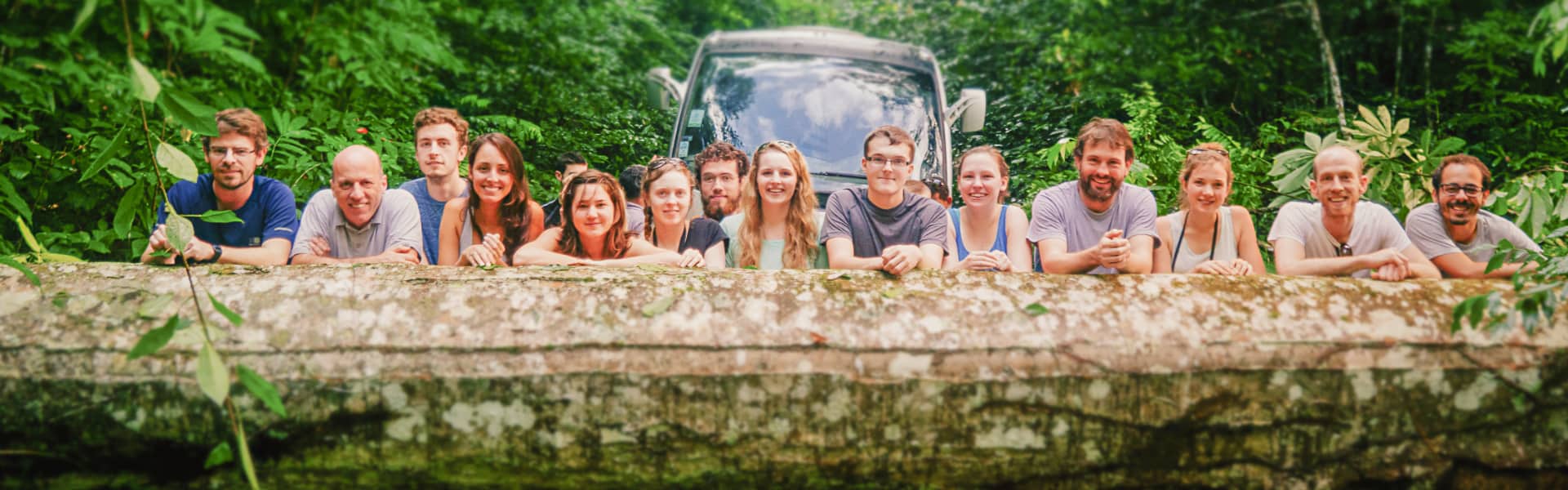 Staff and students on a field trip to the Amazon stand behind a fallen tree.