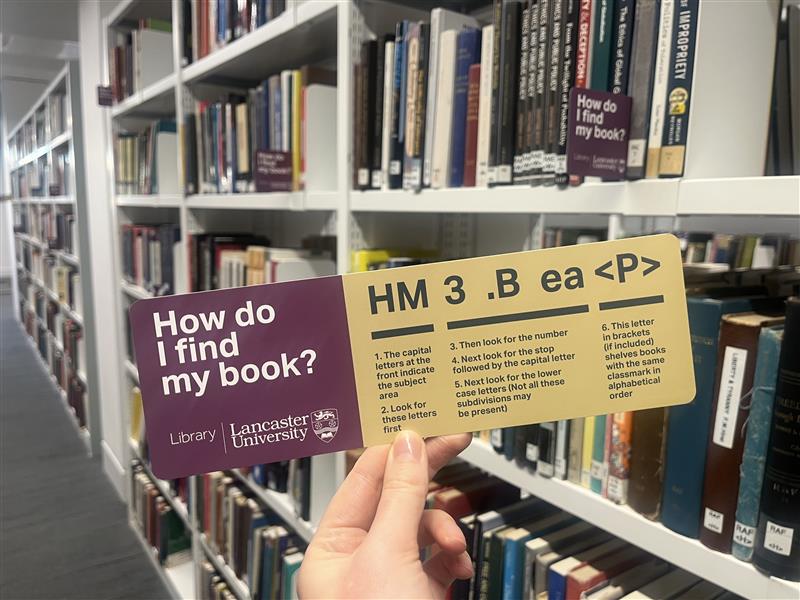 A book finder key being held up in front of a shelf