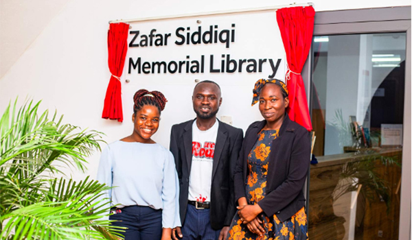 Three members of Lancaster University Ghana Library team standing at the library entrance.